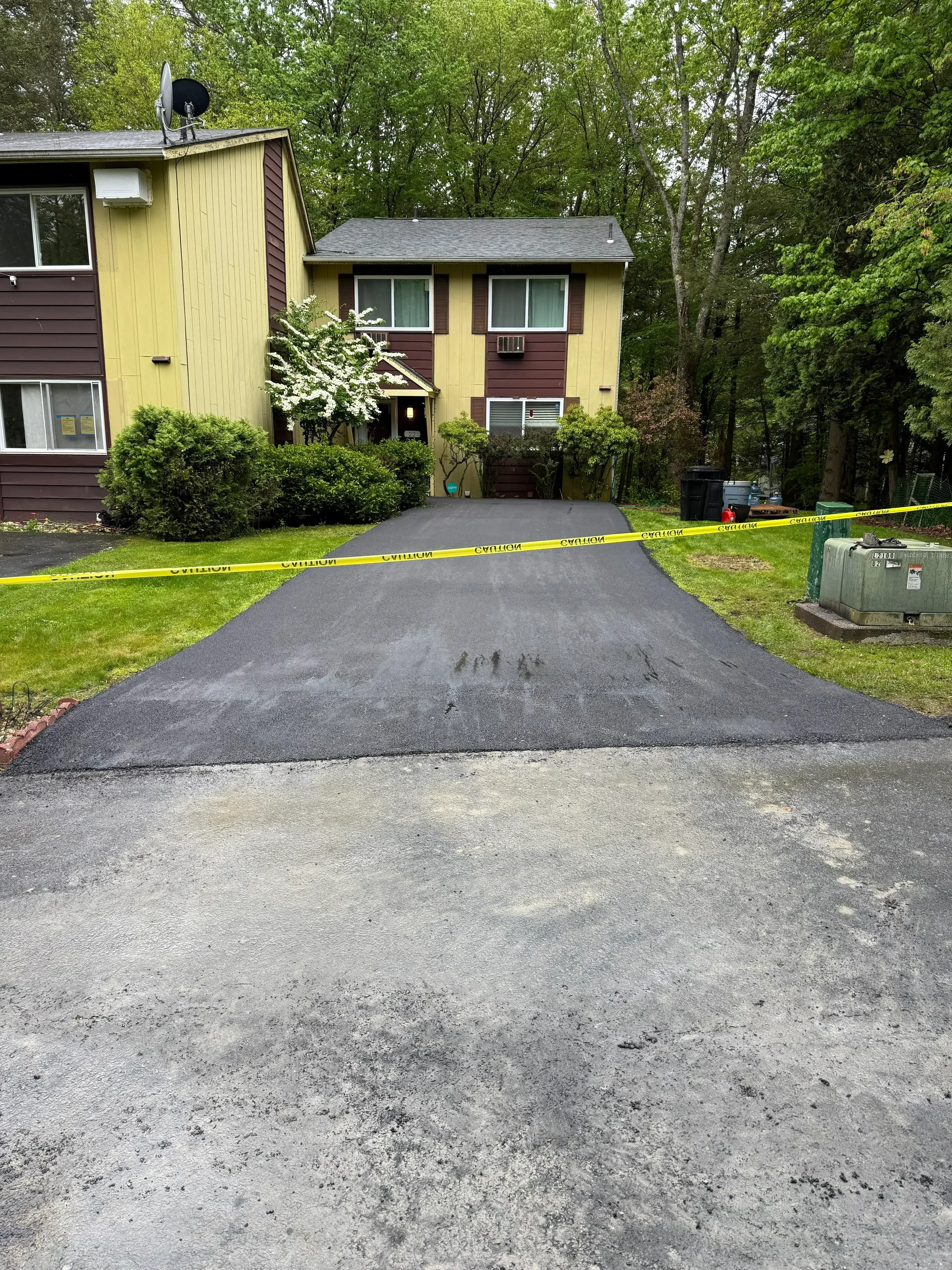 Fresh asphalt driveway with clean edges alongside residential home with yellow siding