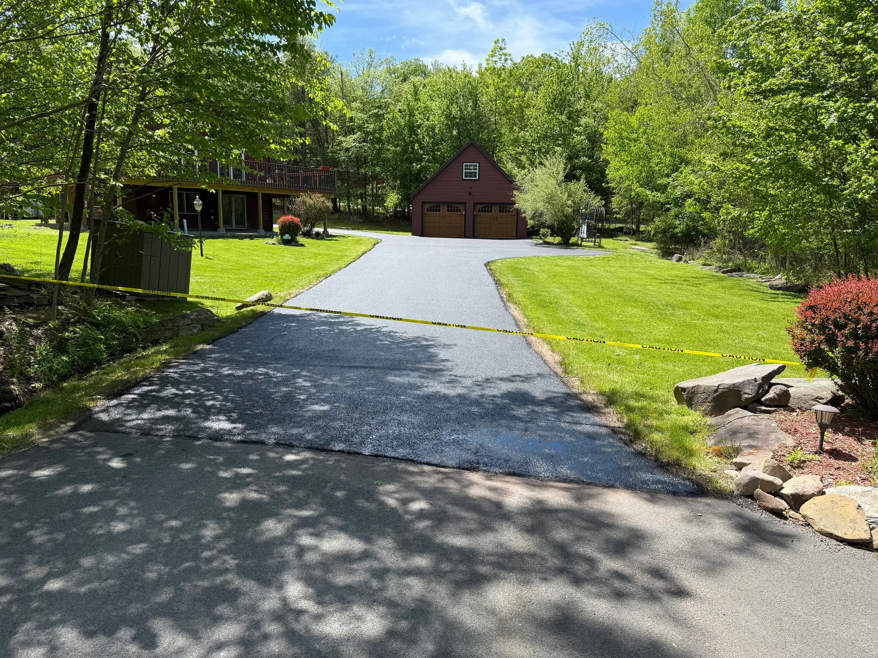 Curved asphalt driveway with fresh paving leading to two-car garage on wooded property