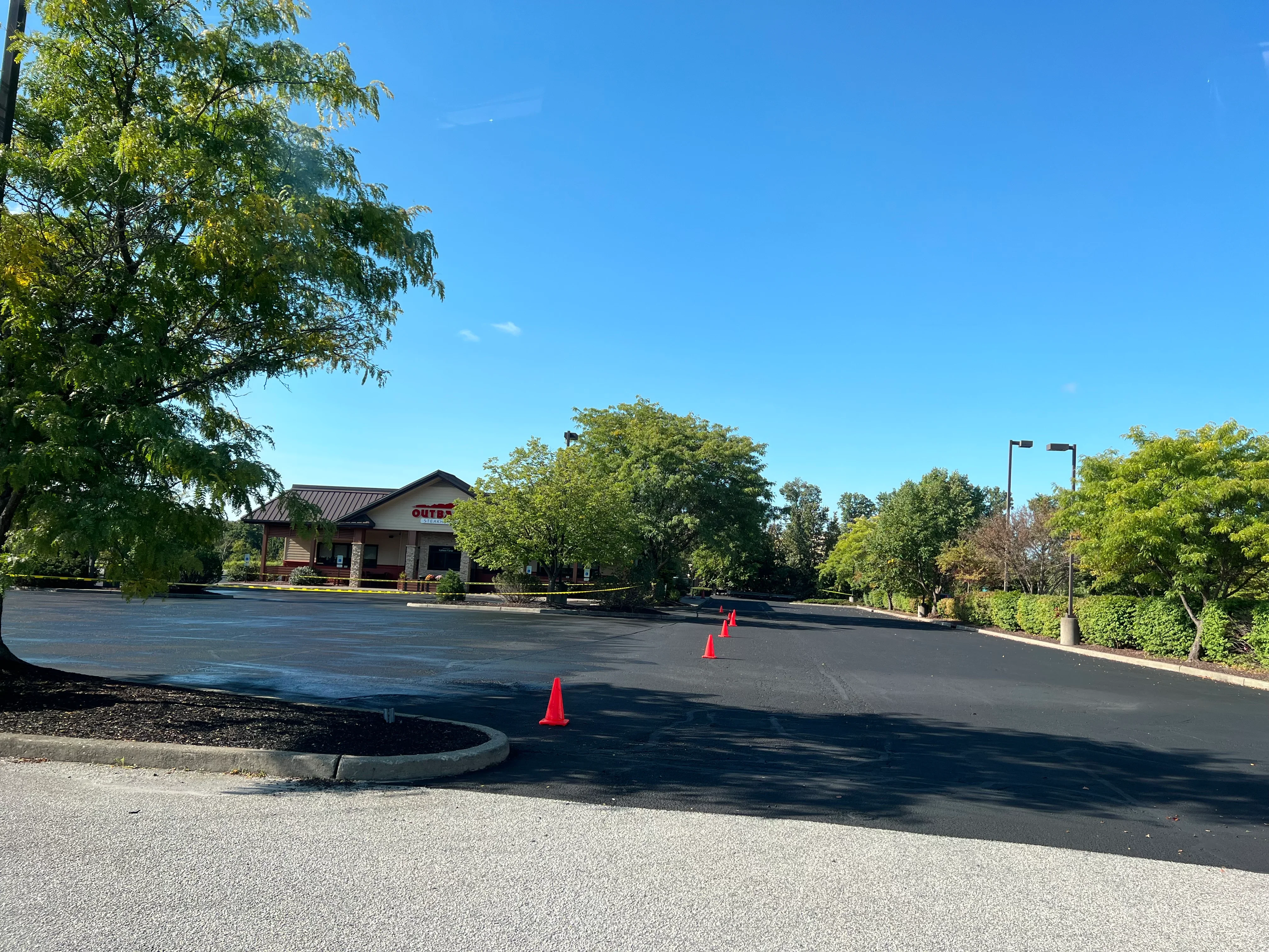 Newly paved commercial parking lot with fresh black asphalt, concrete curbing, and traffic cones