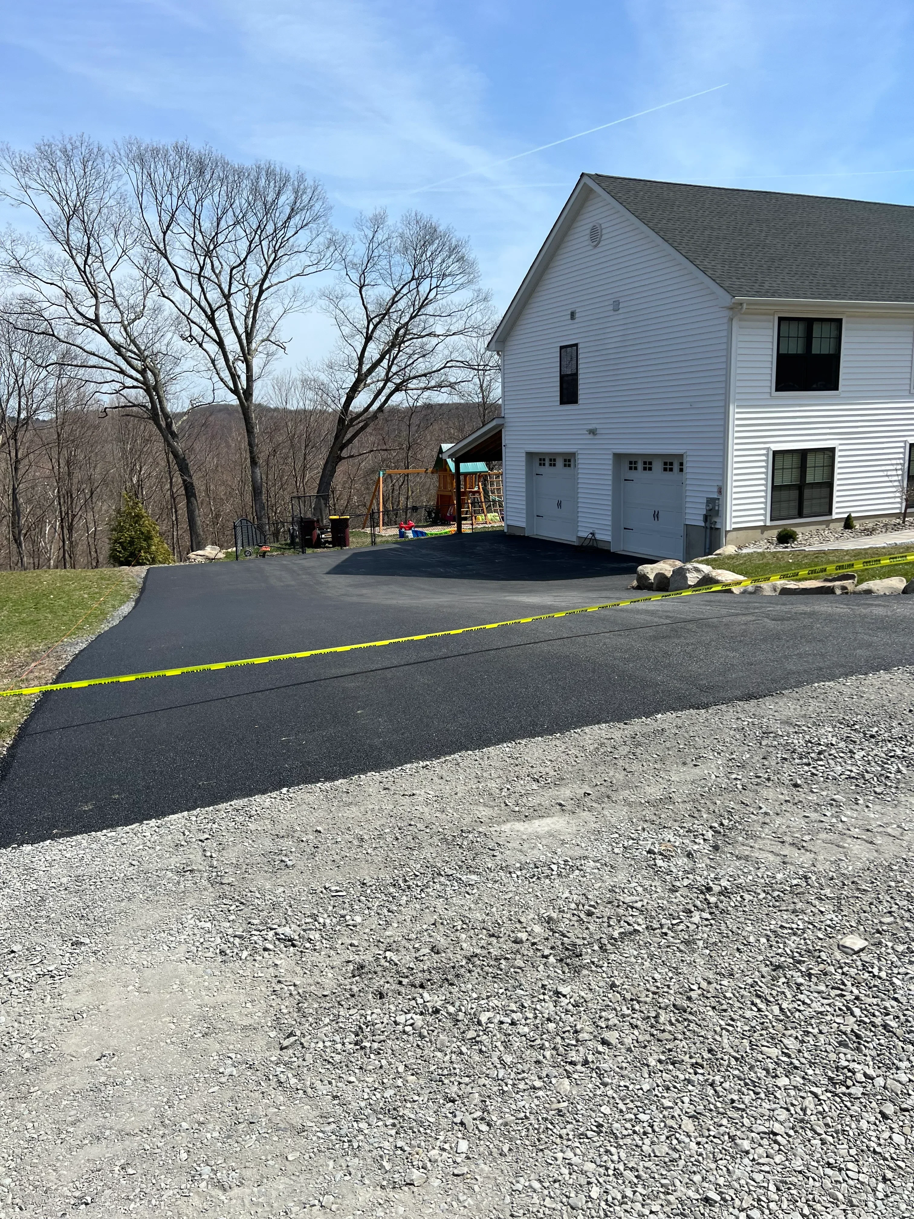 Newly paved asphalt driveway with yellow line striping adjacent to brick building