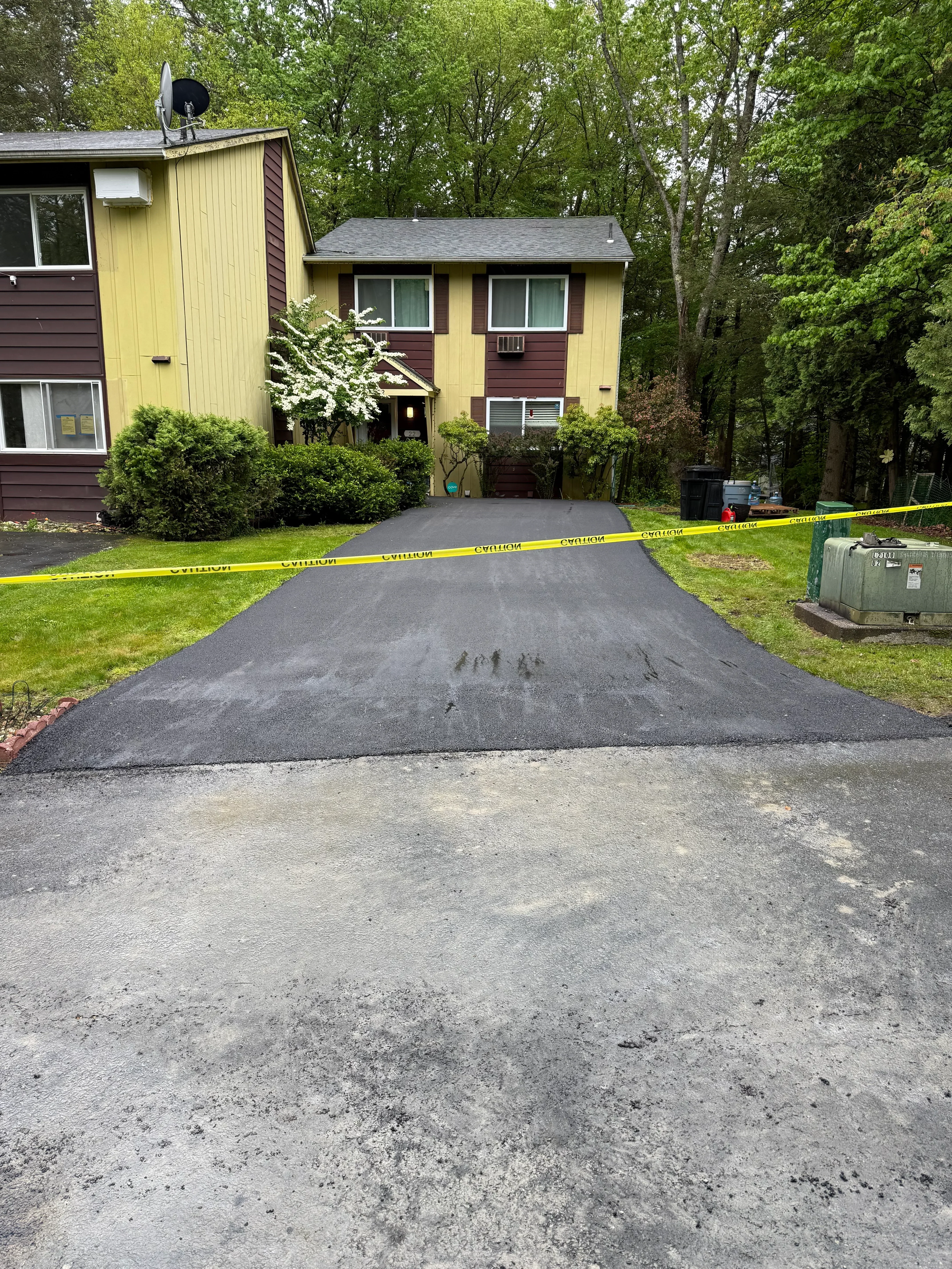 New asphalt driveway installed at residential home with yellow siding and landscaping