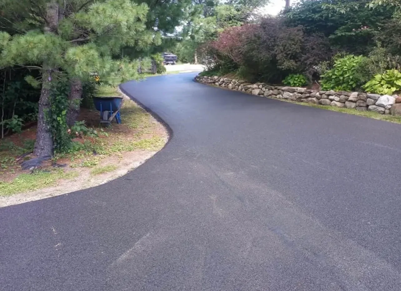 Newly paved curved asphalt driveway with stone retaining wall and mature trees