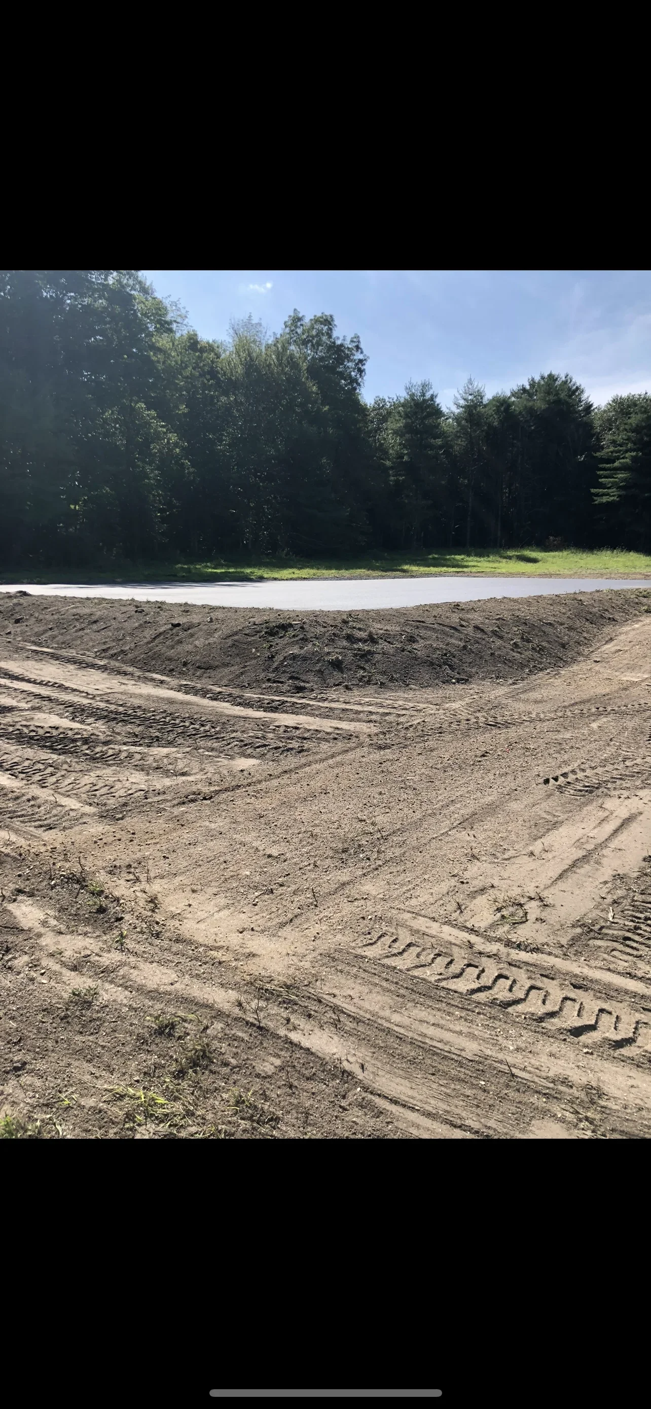 Excavated driveway site with graded soil base, drainage swale, and compacted subgrade ready for asphalt