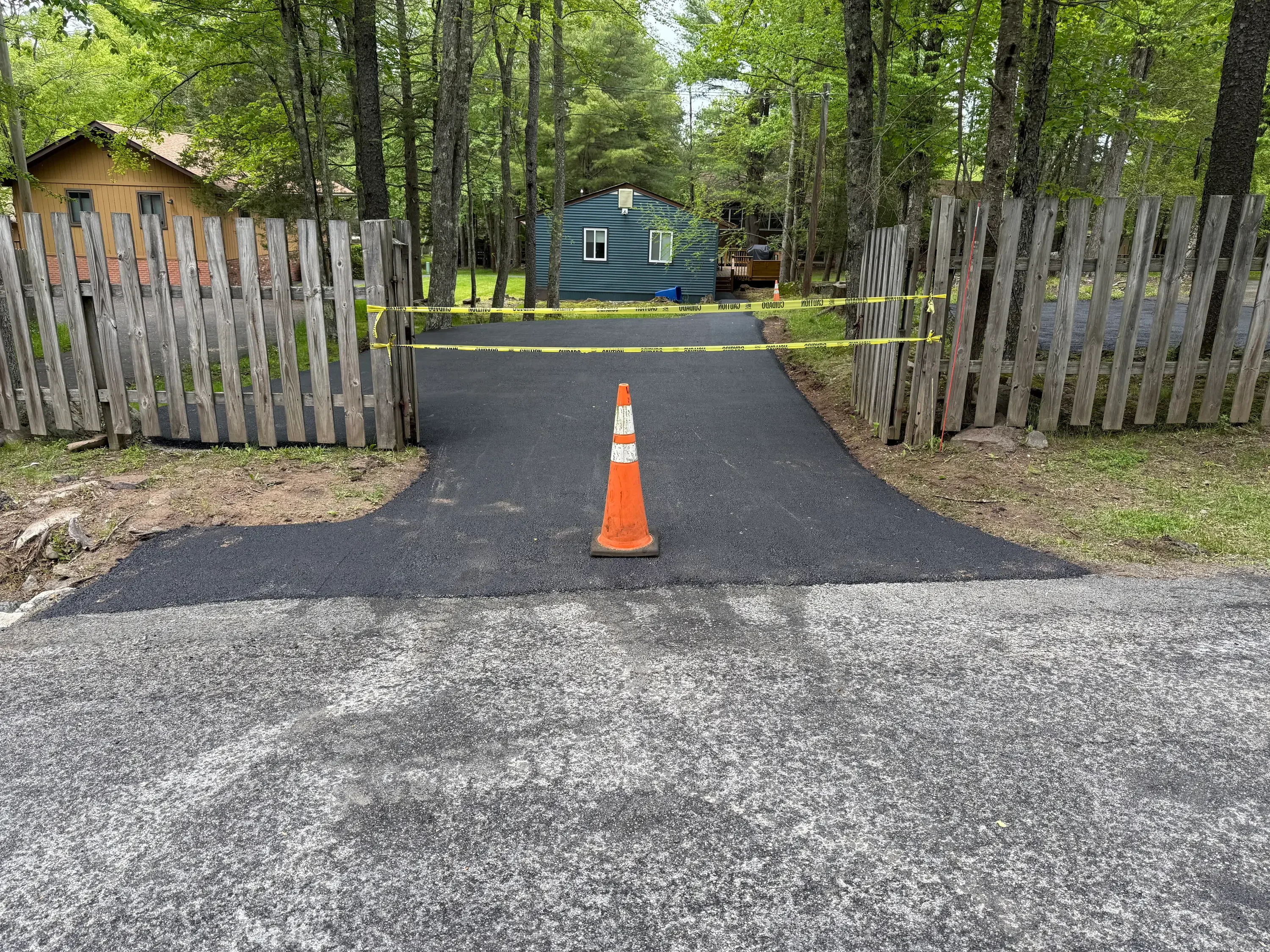New black asphalt driveway with orange traffic cone, wooden fence gates on sides