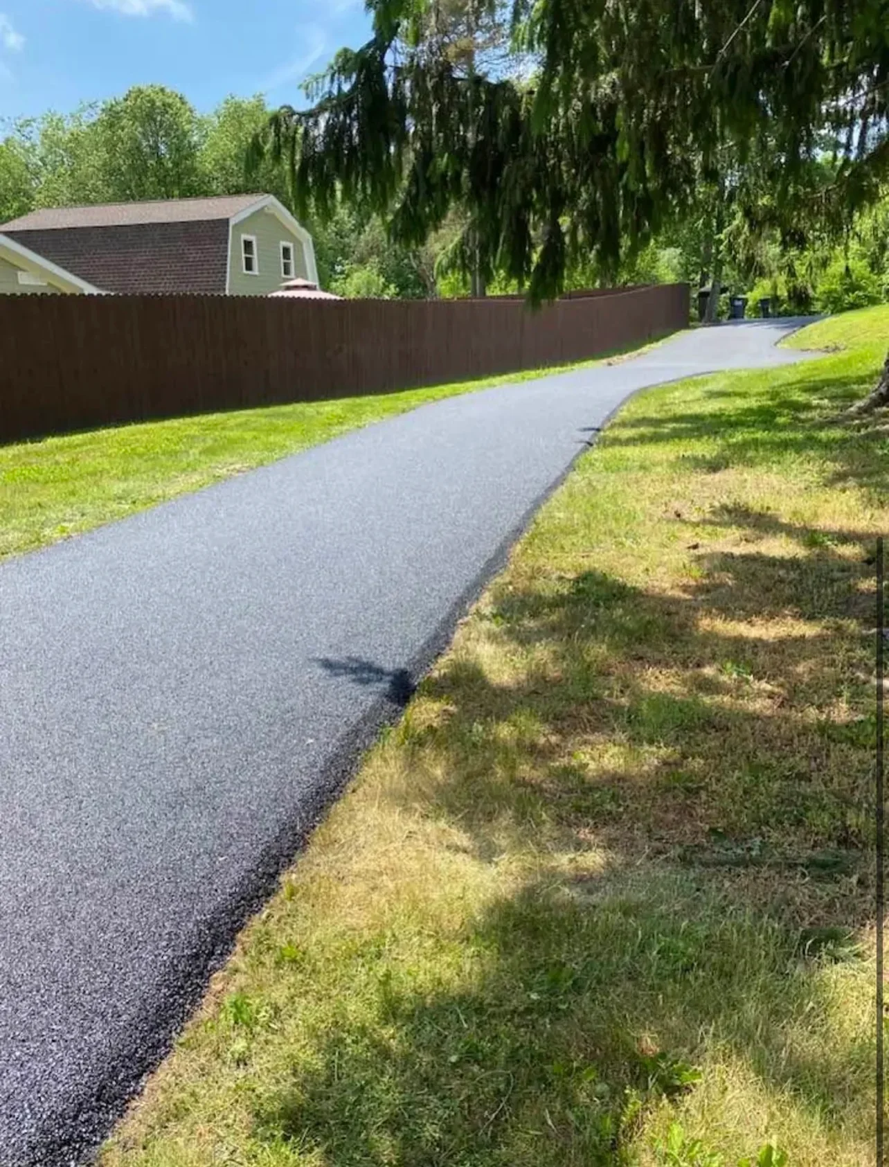 Newly paved asphalt driveway with dark surface and clean edges bordering manicured lawn