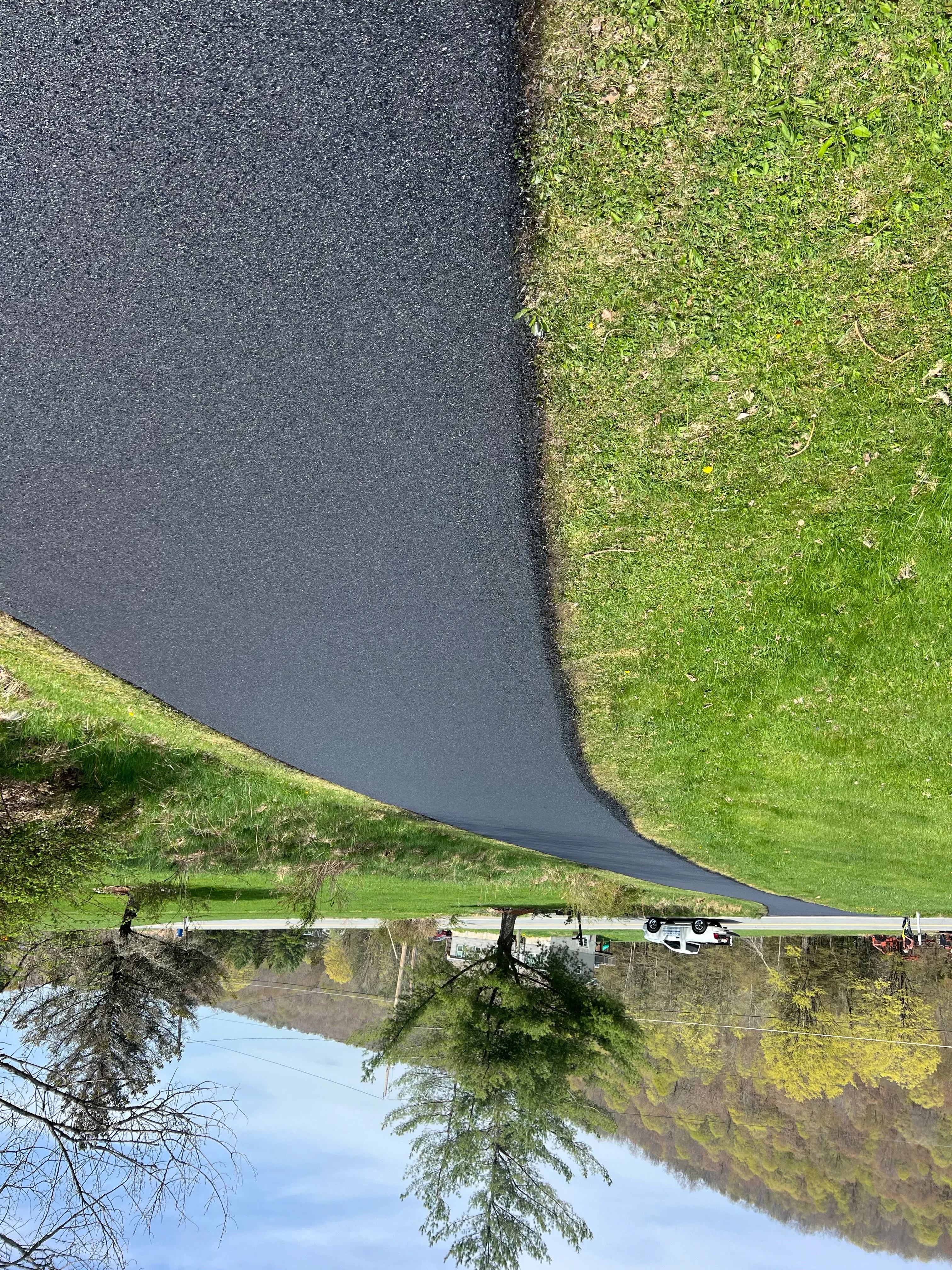 Newly installed black asphalt driveway with clean edges adjacent to green lawn