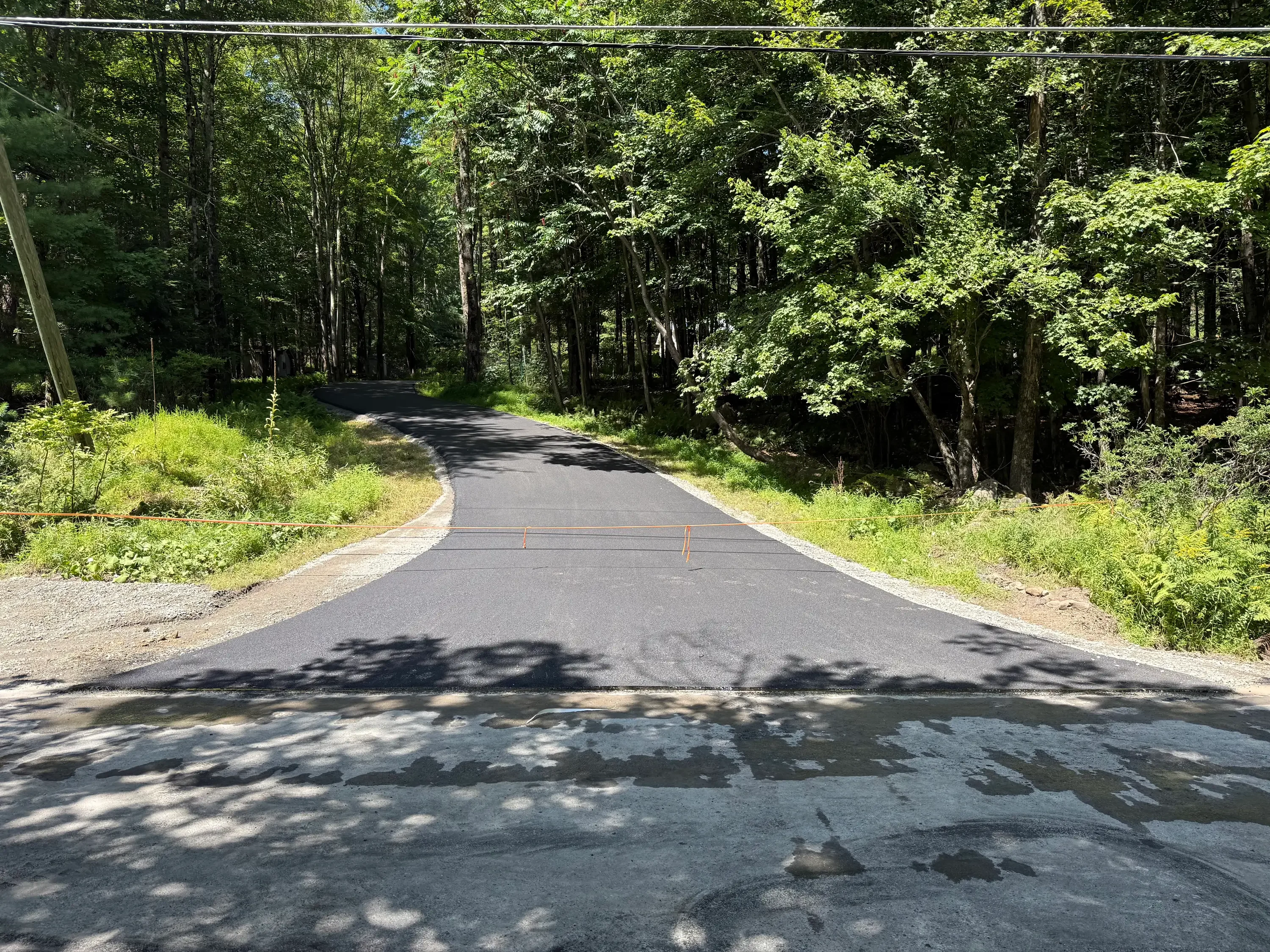 Newly paved black asphalt driveway with gravel edges through wooded area