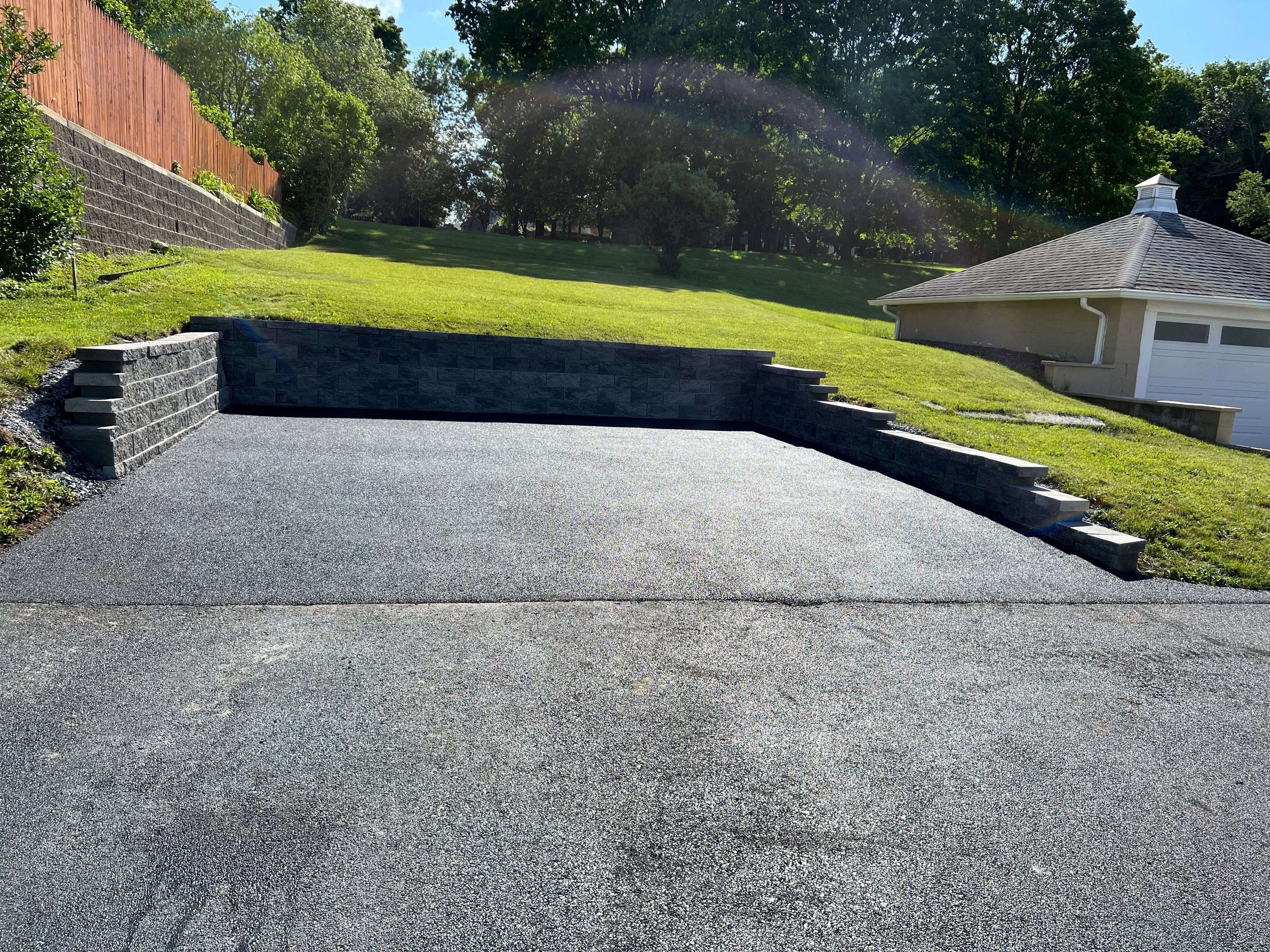 Asphalt driveway with black retaining wall on sloped residential lot