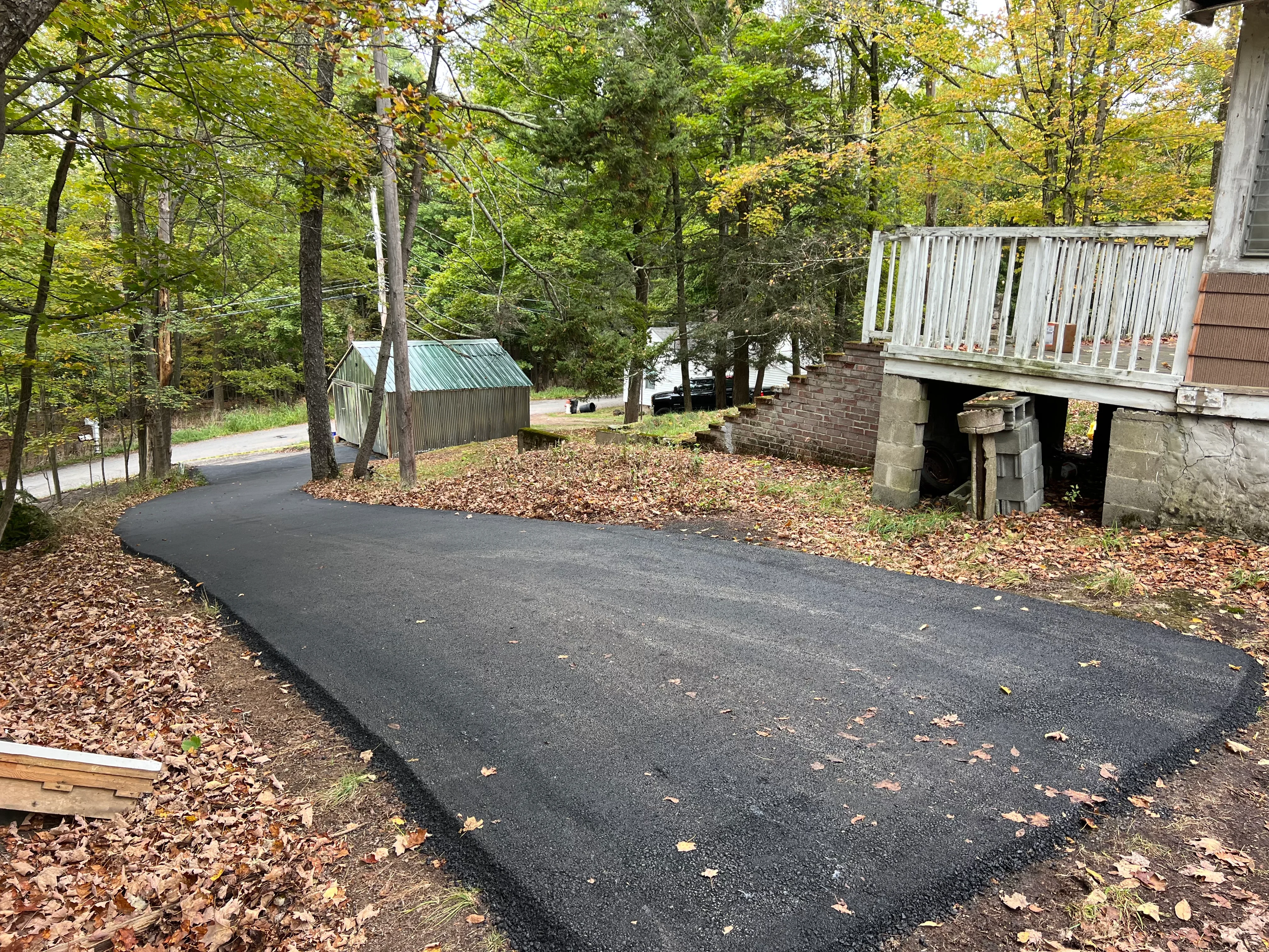 New black asphalt driveway with curved layout through wooded residential property