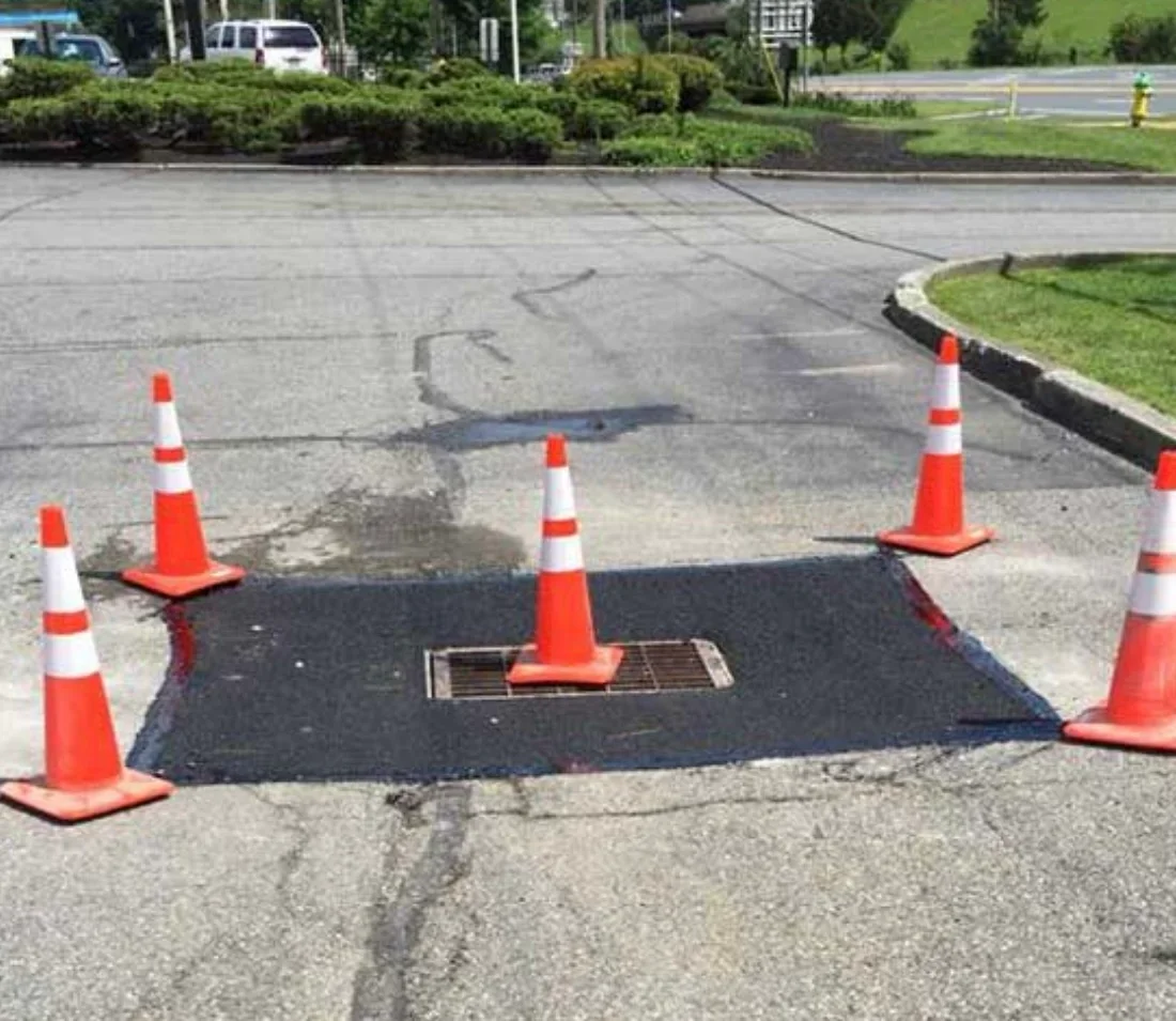 Catch basin installation with asphalt patch and traffic cones on parking lot