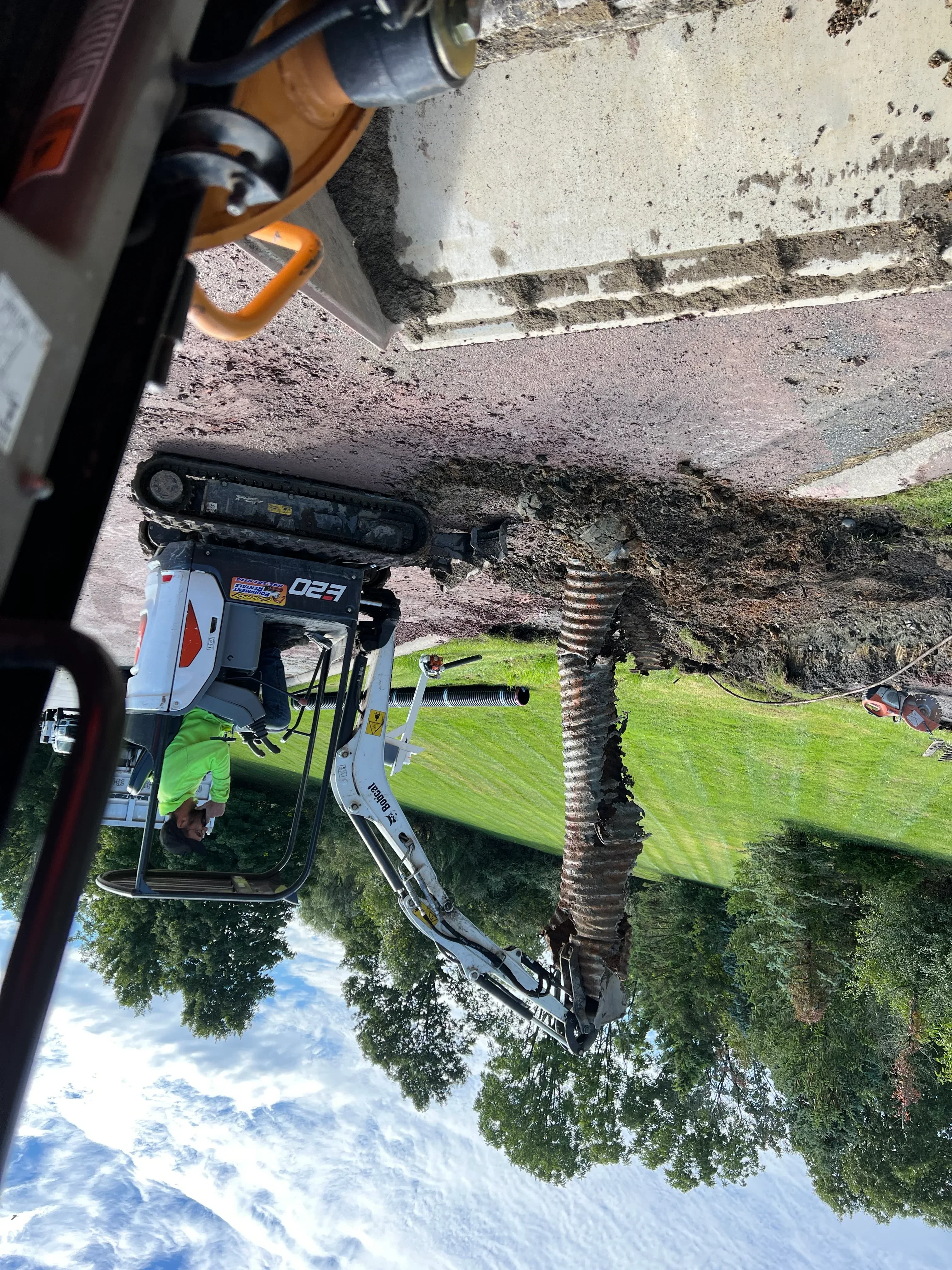 Compact track loader excavating and grading driveway site with corrugated drainage pipe