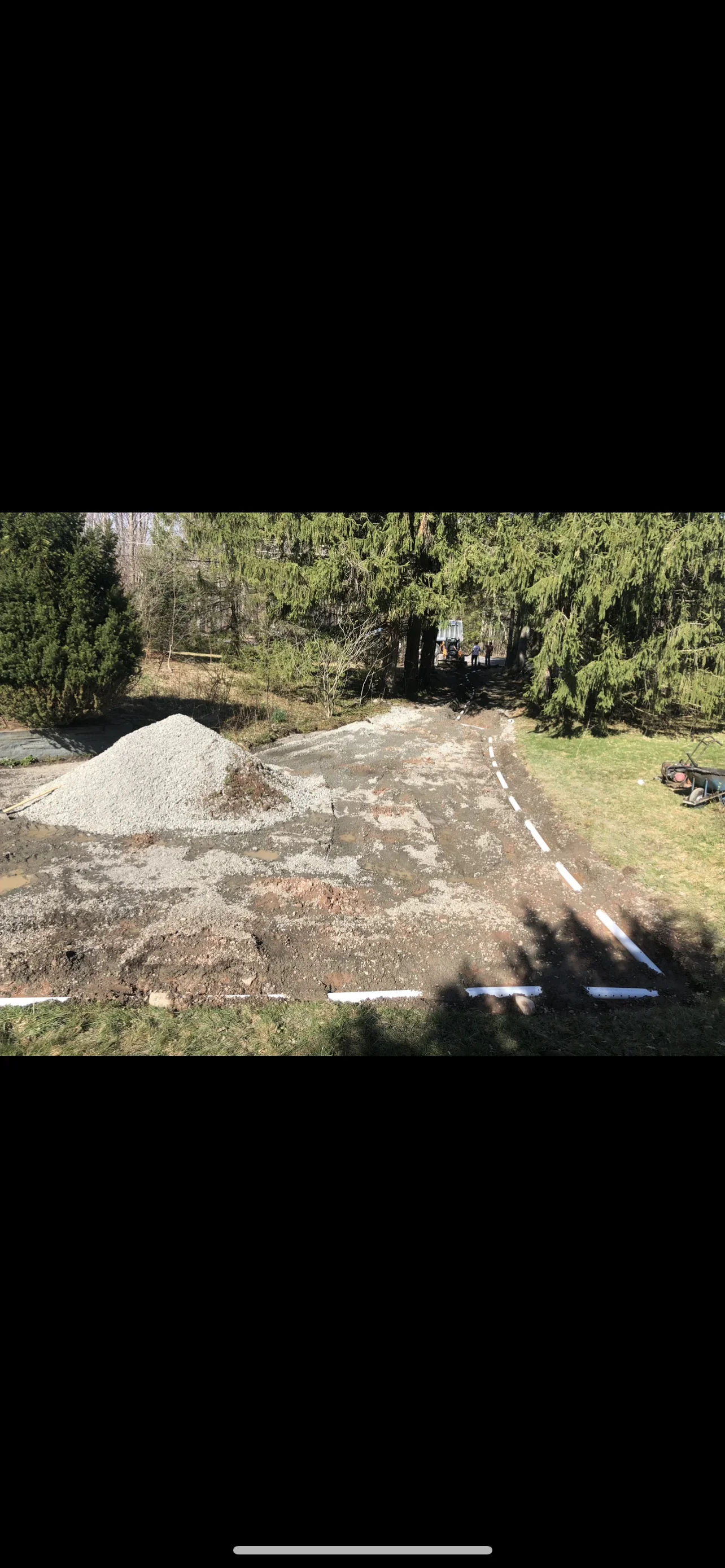 Excavated driveway site with gravel base pile and blue layout lines on prepared ground