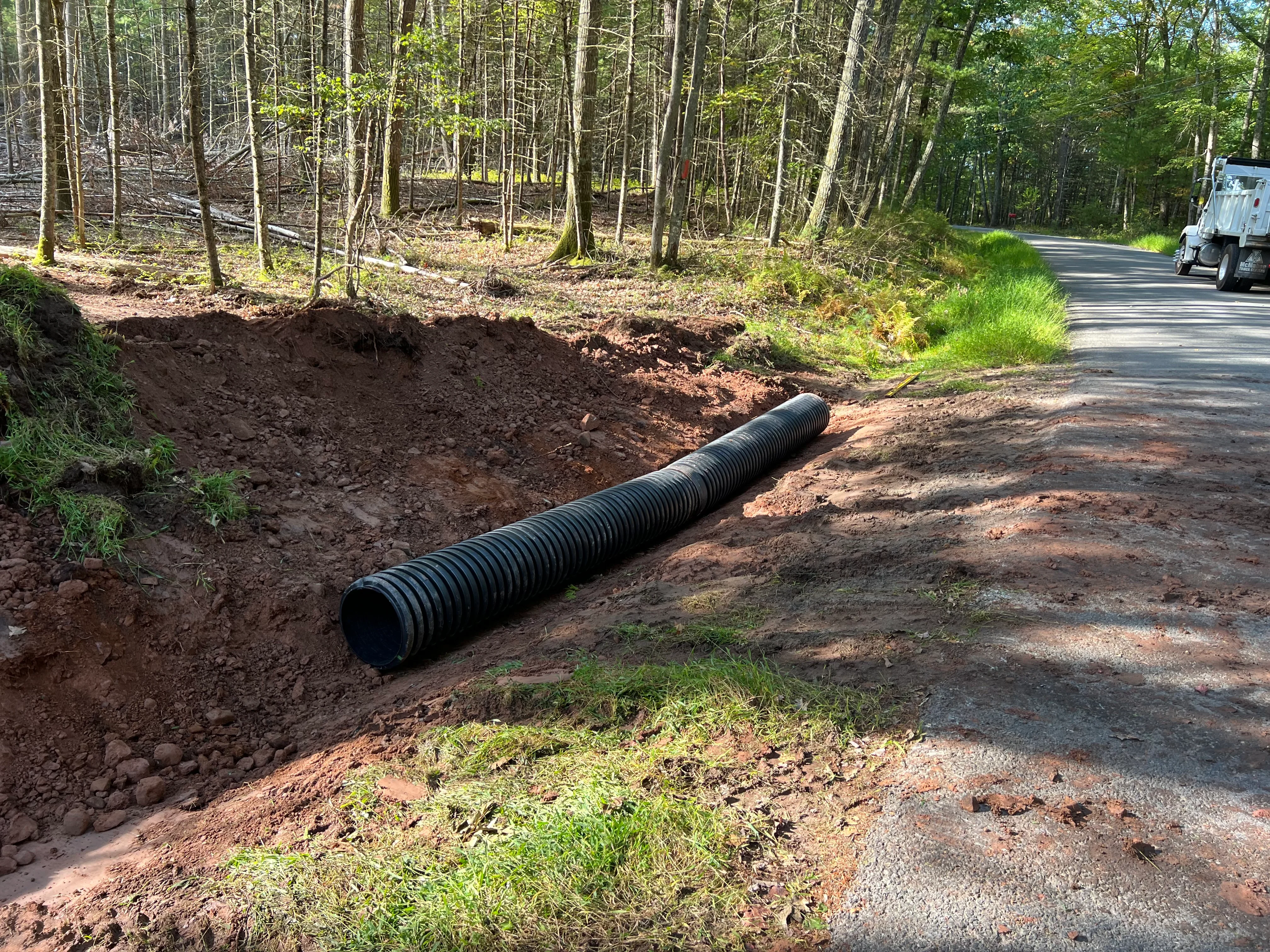Black corrugated drainage pipe installed in excavated trench alongside driveway