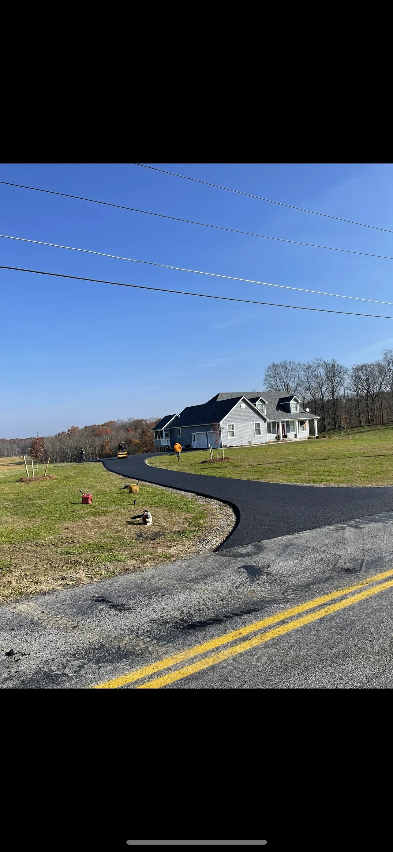 Curved black asphalt driveway with fresh paving leading to residential home