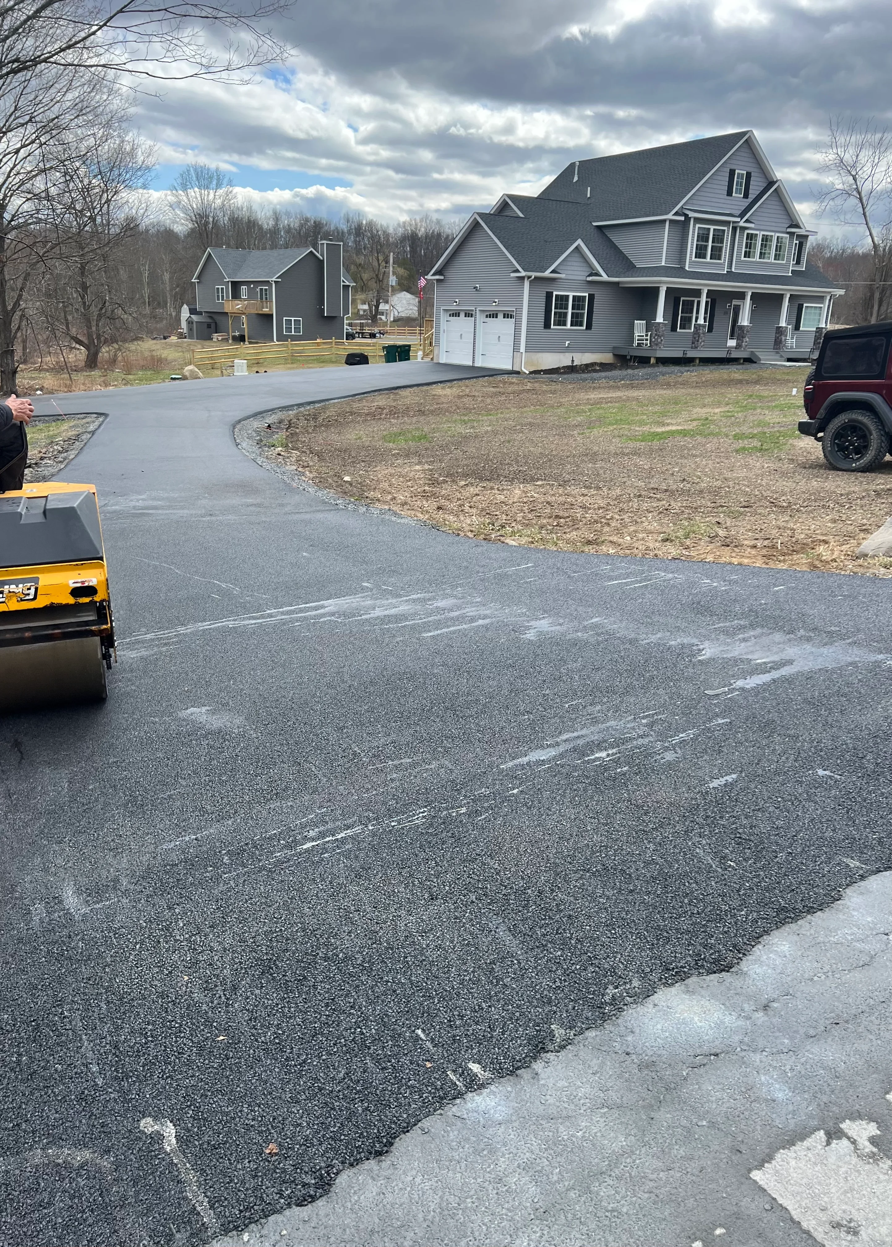 Newly paved asphalt driveway with curved design and compaction roller on-site