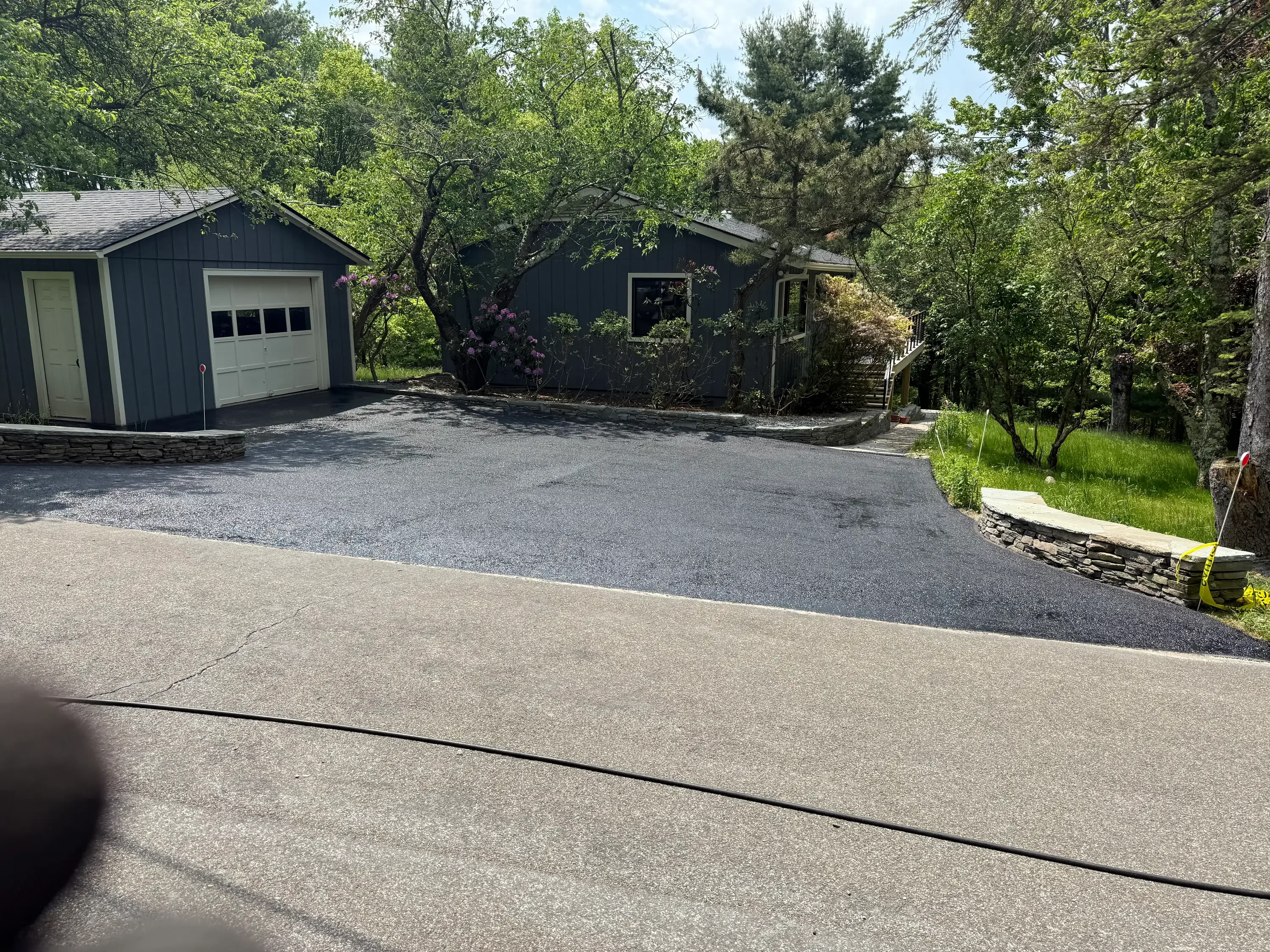 Newly paved asphalt driveway with concrete apron and dark asphalt surface