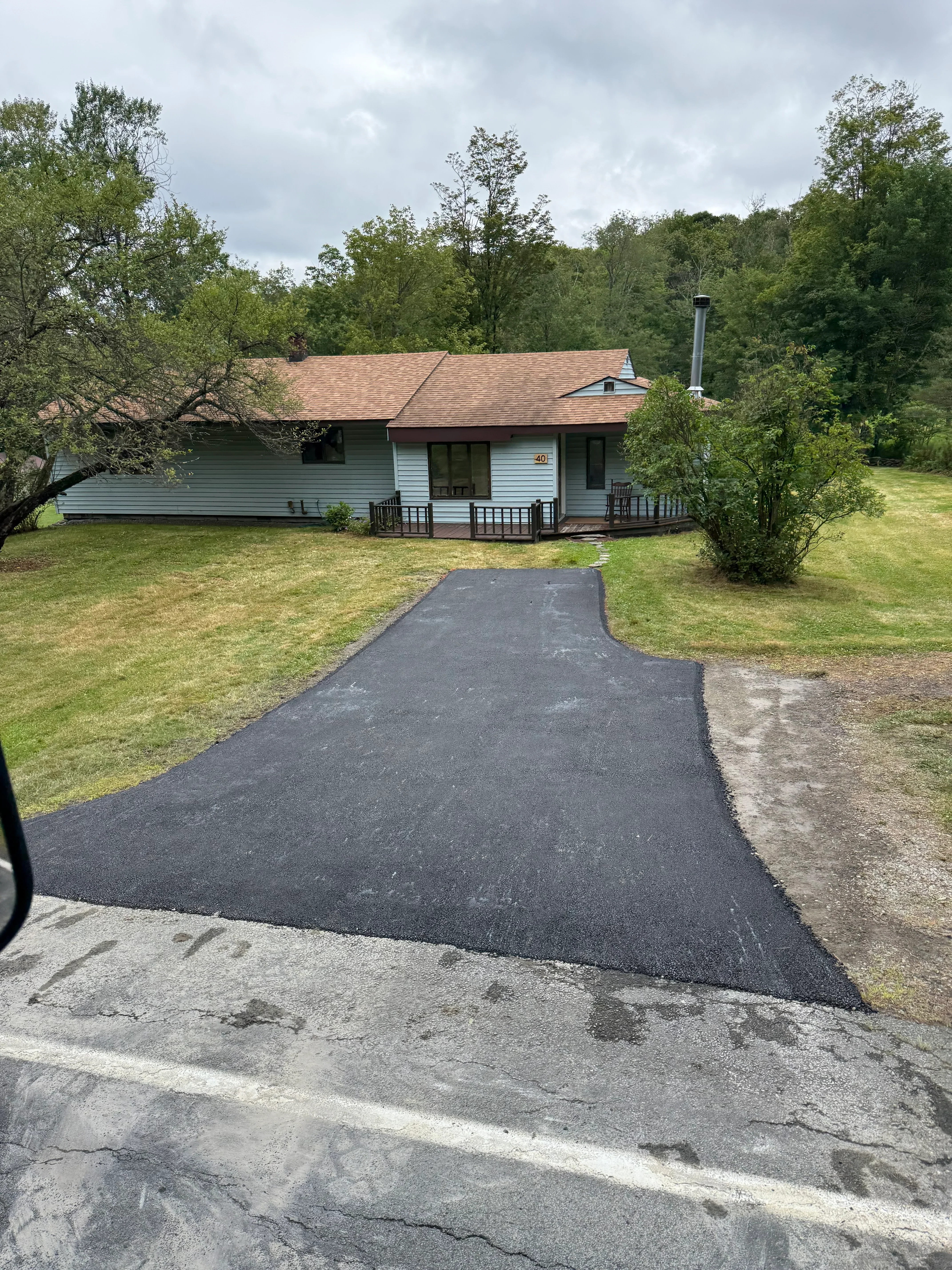 Newly paved black asphalt driveway alongside brick residential home with green lawn