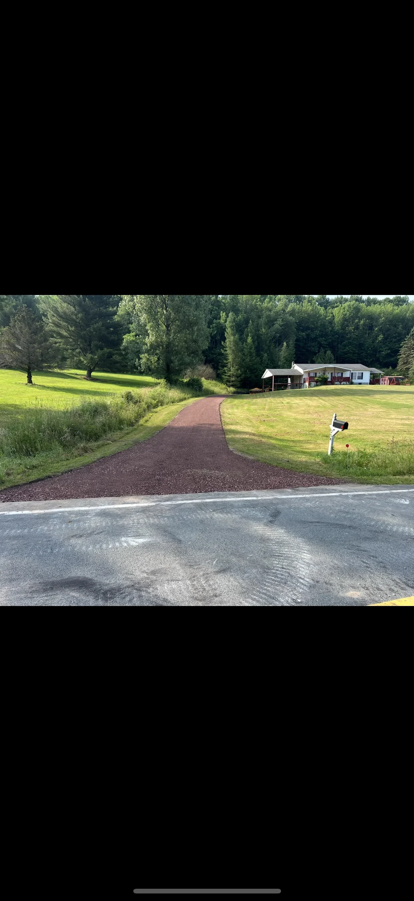 New dark asphalt driveway with curved design on residential property with mailbox