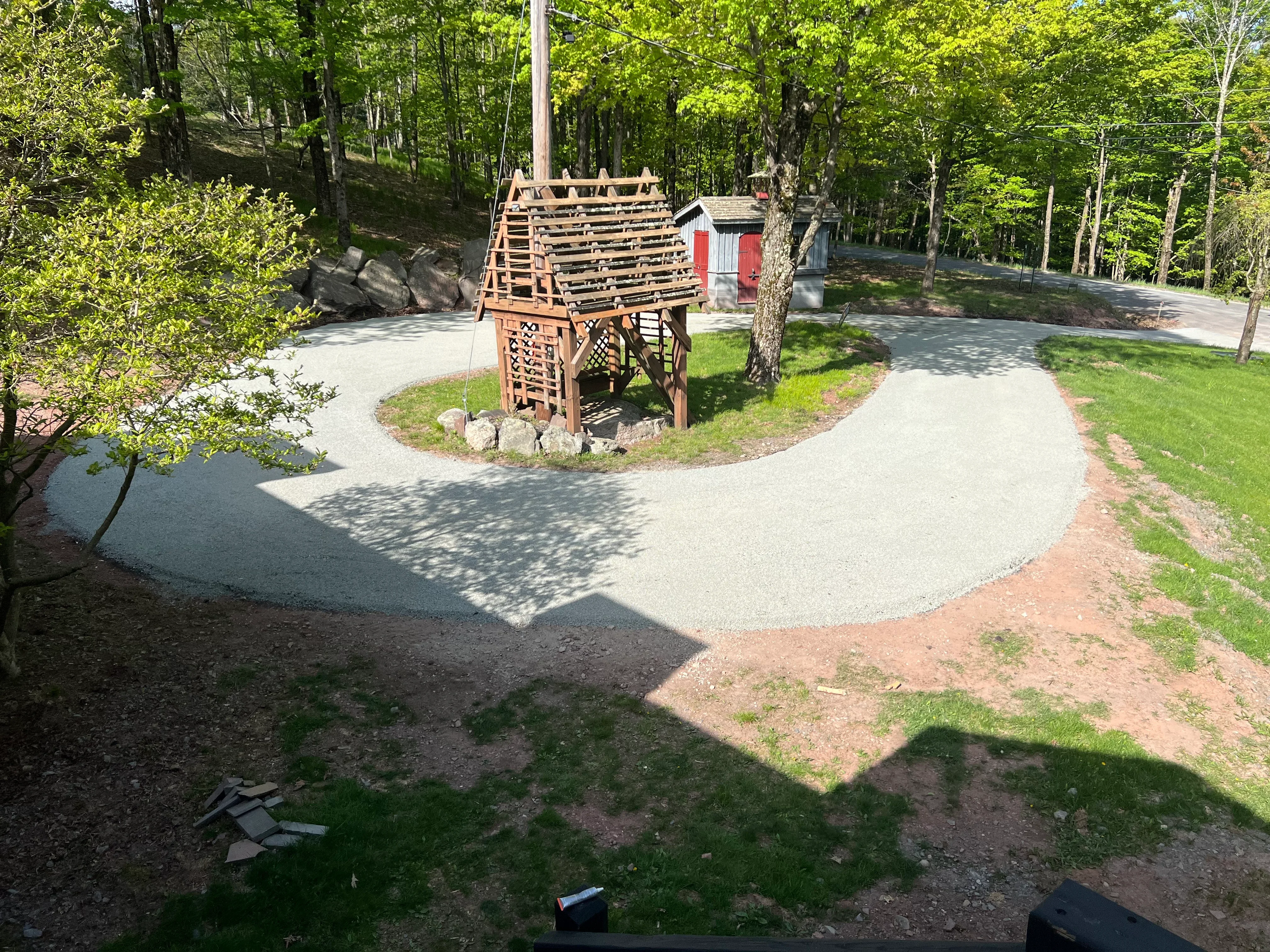 Curved gravel driveway with asphalt base, stone edging, and mature trees in wooded setting
