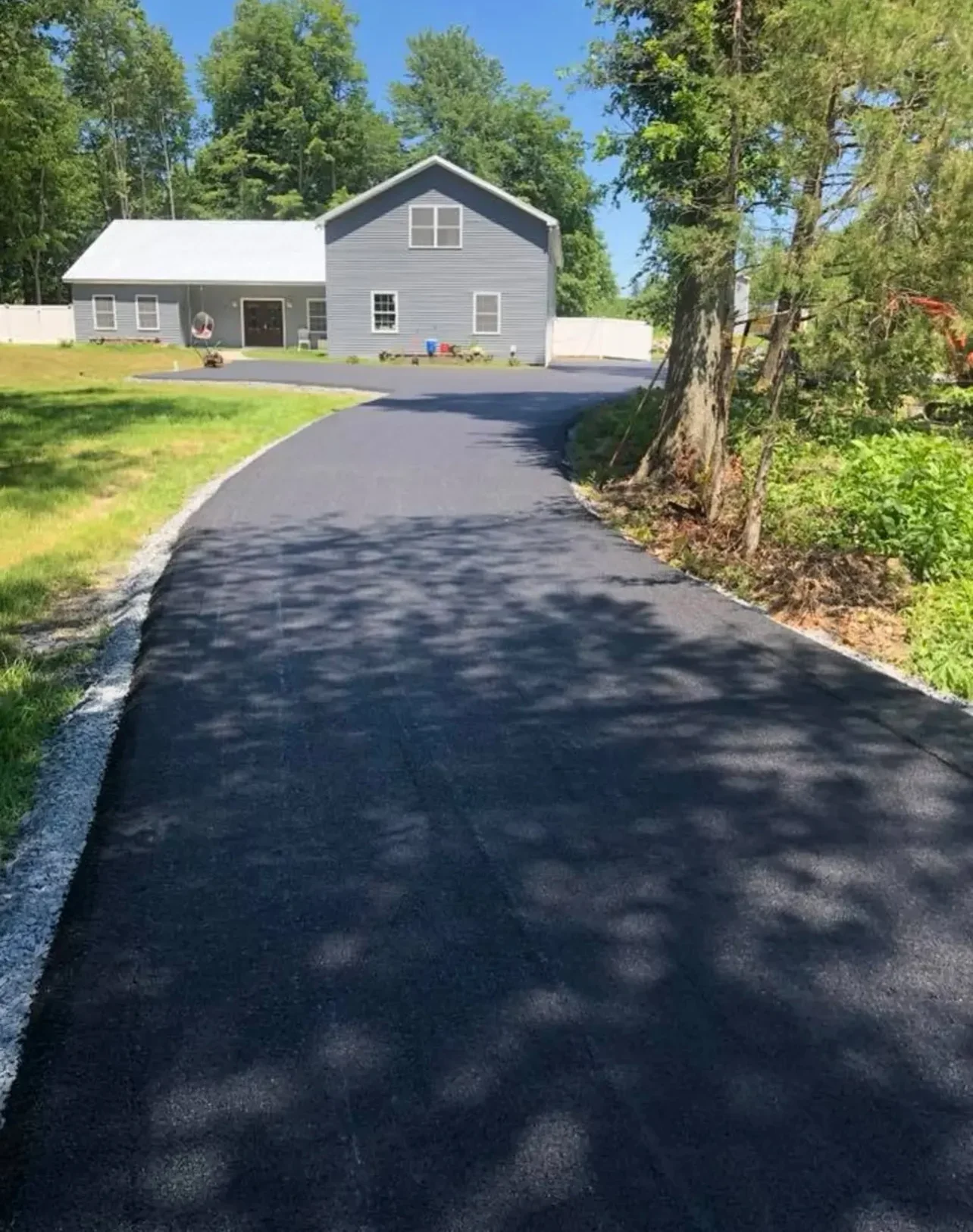 Newly paved black asphalt driveway with gravel borders and curved approach to gray residential home