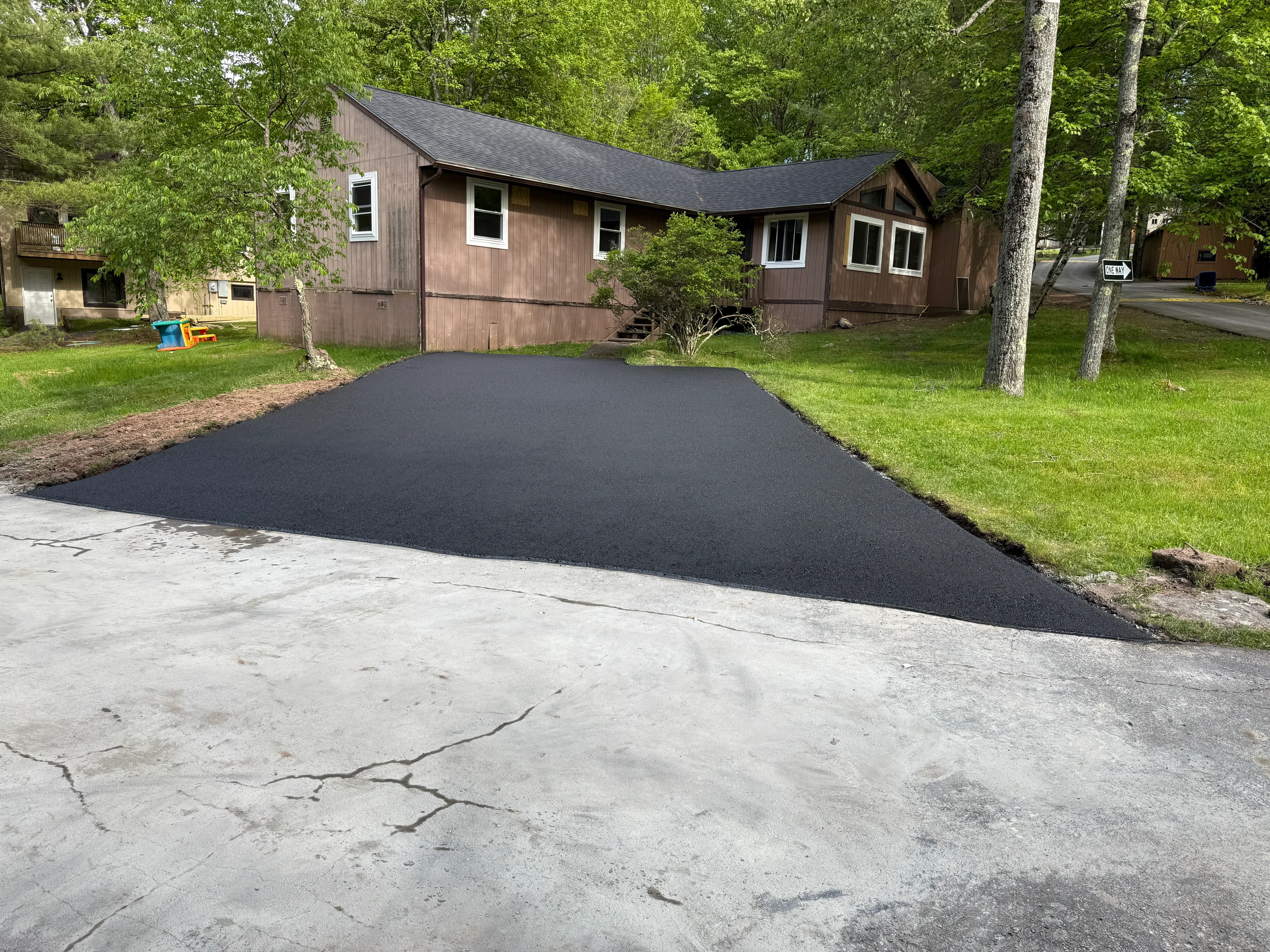 New black asphalt driveway with concrete apron transition and lawn borders