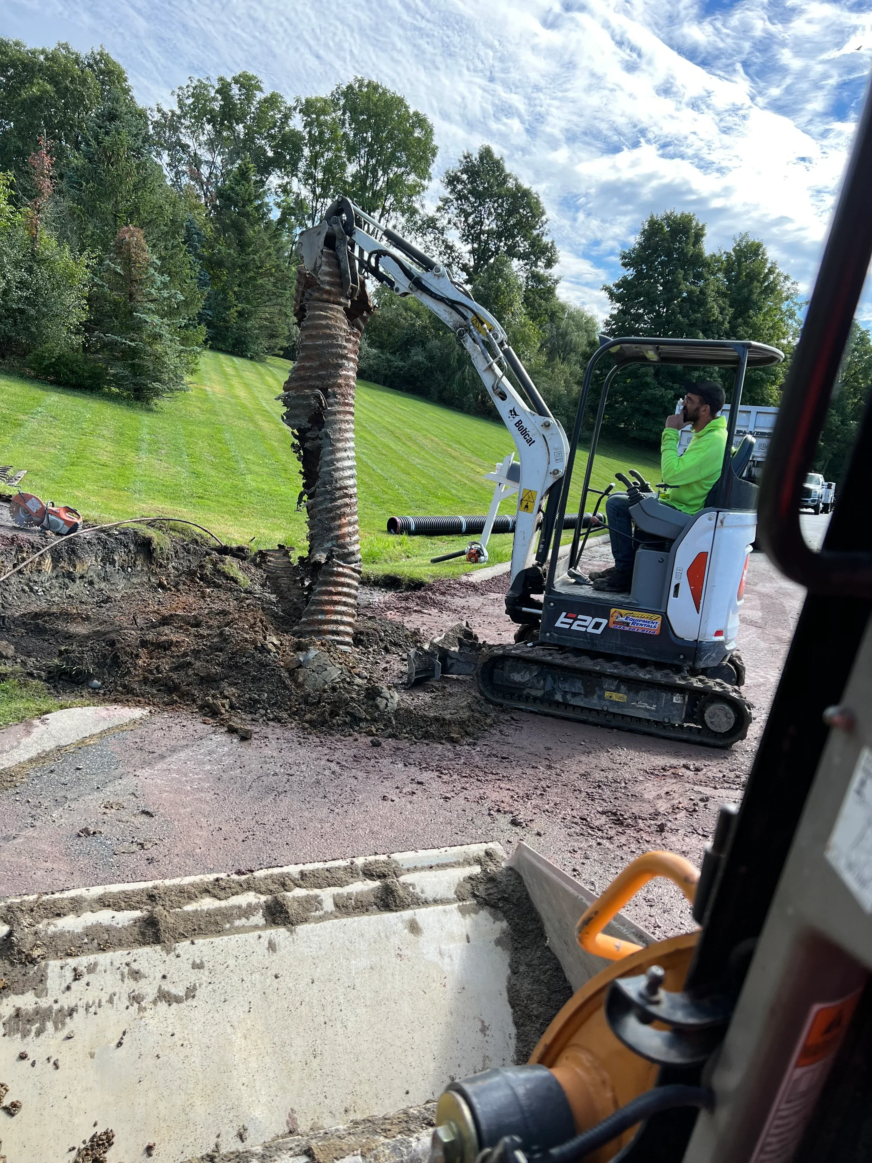 Compact track loader excavating and grading driveway site with corrugated drainage pipe