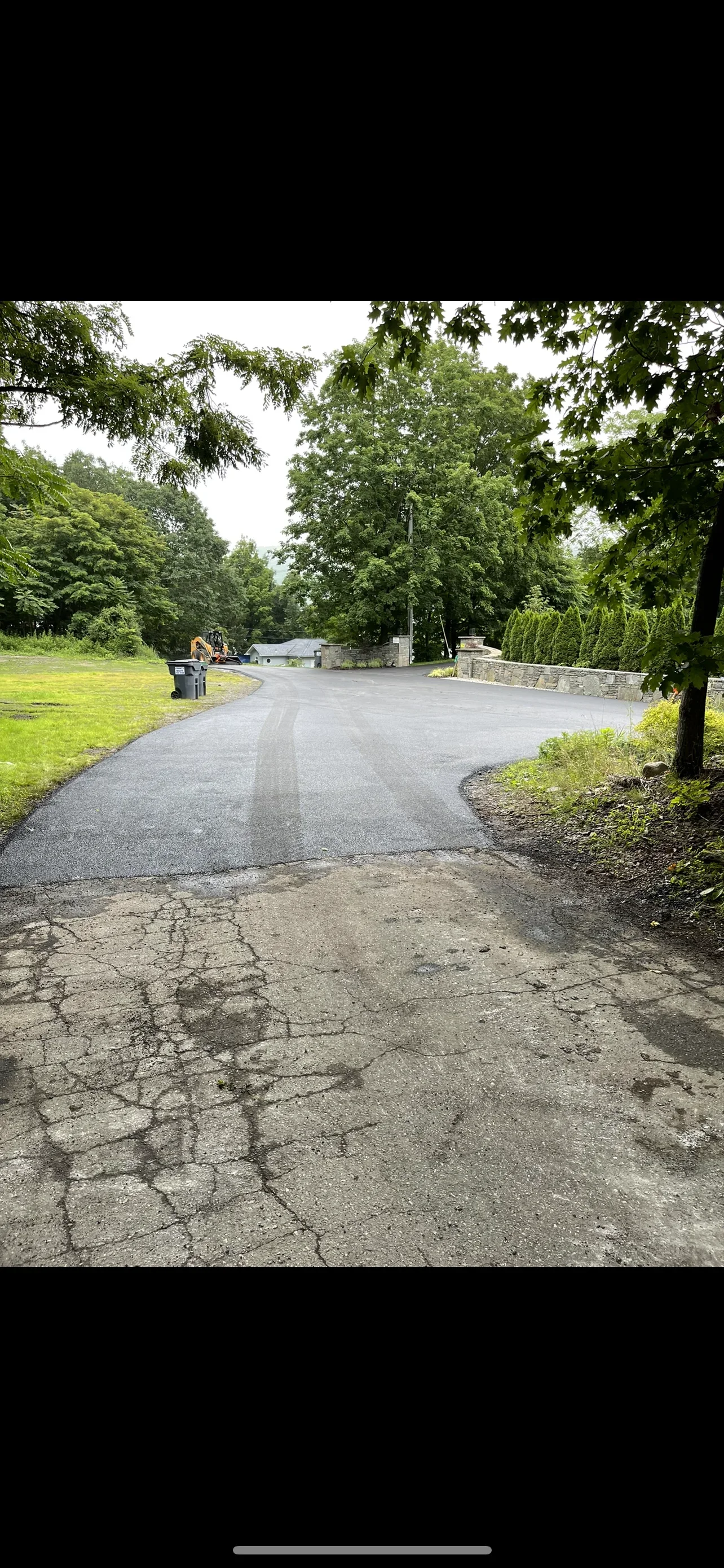 New asphalt driveway with curved layout, mature trees, and stone retaining wall