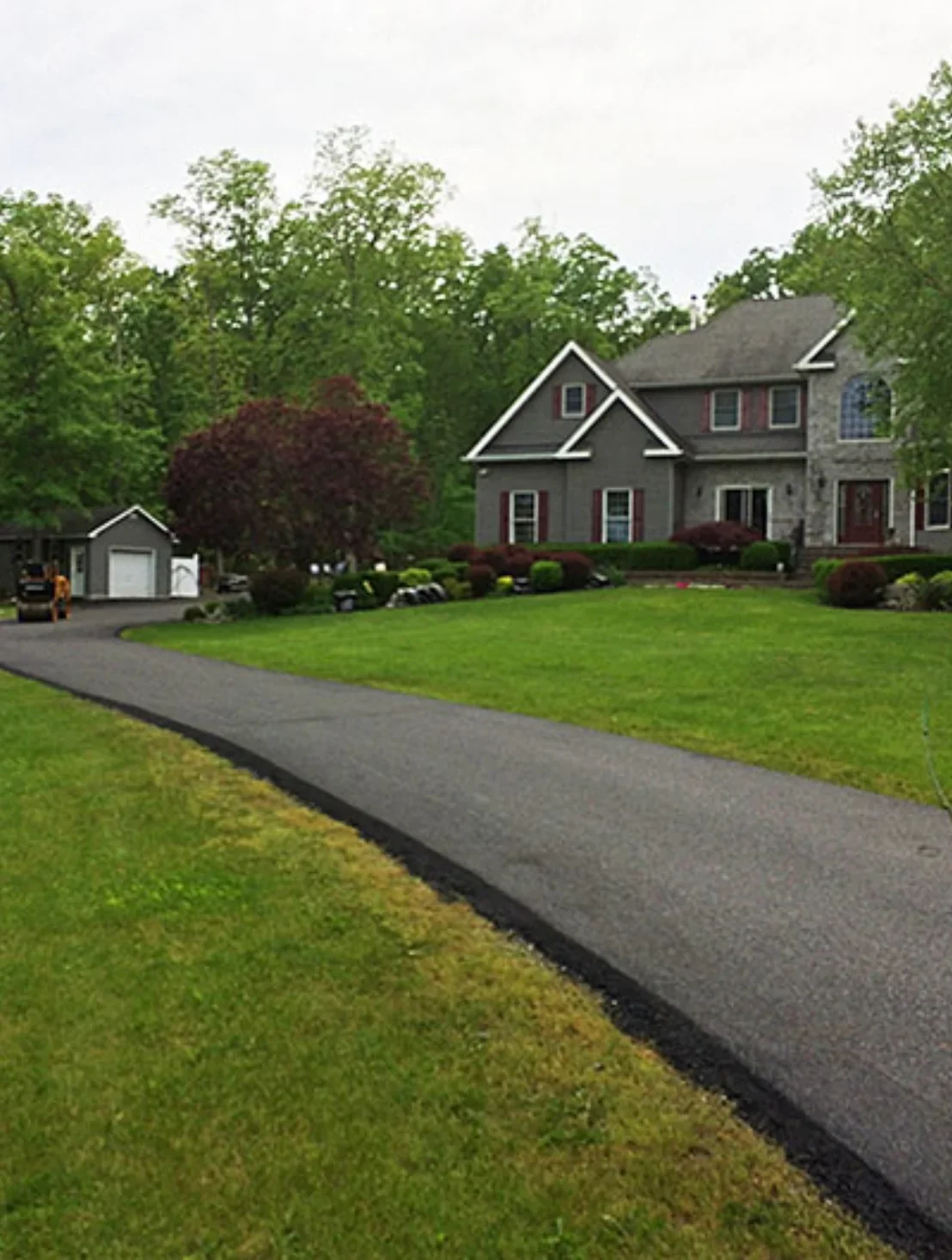 New asphalt driveway with clean edges leading to residential home with landscaping