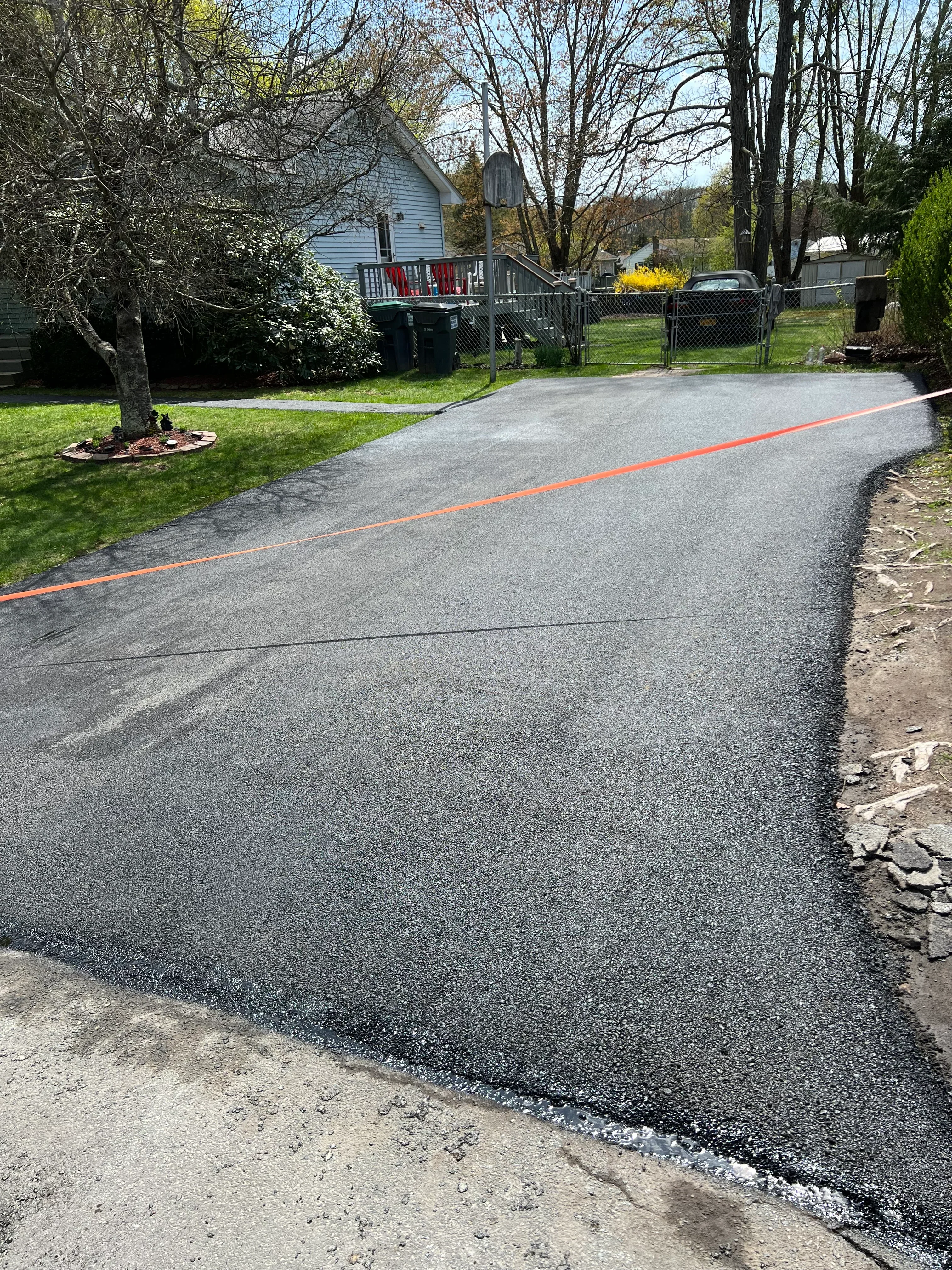 Newly paved asphalt driveway with orange chalk line marking and concrete transition