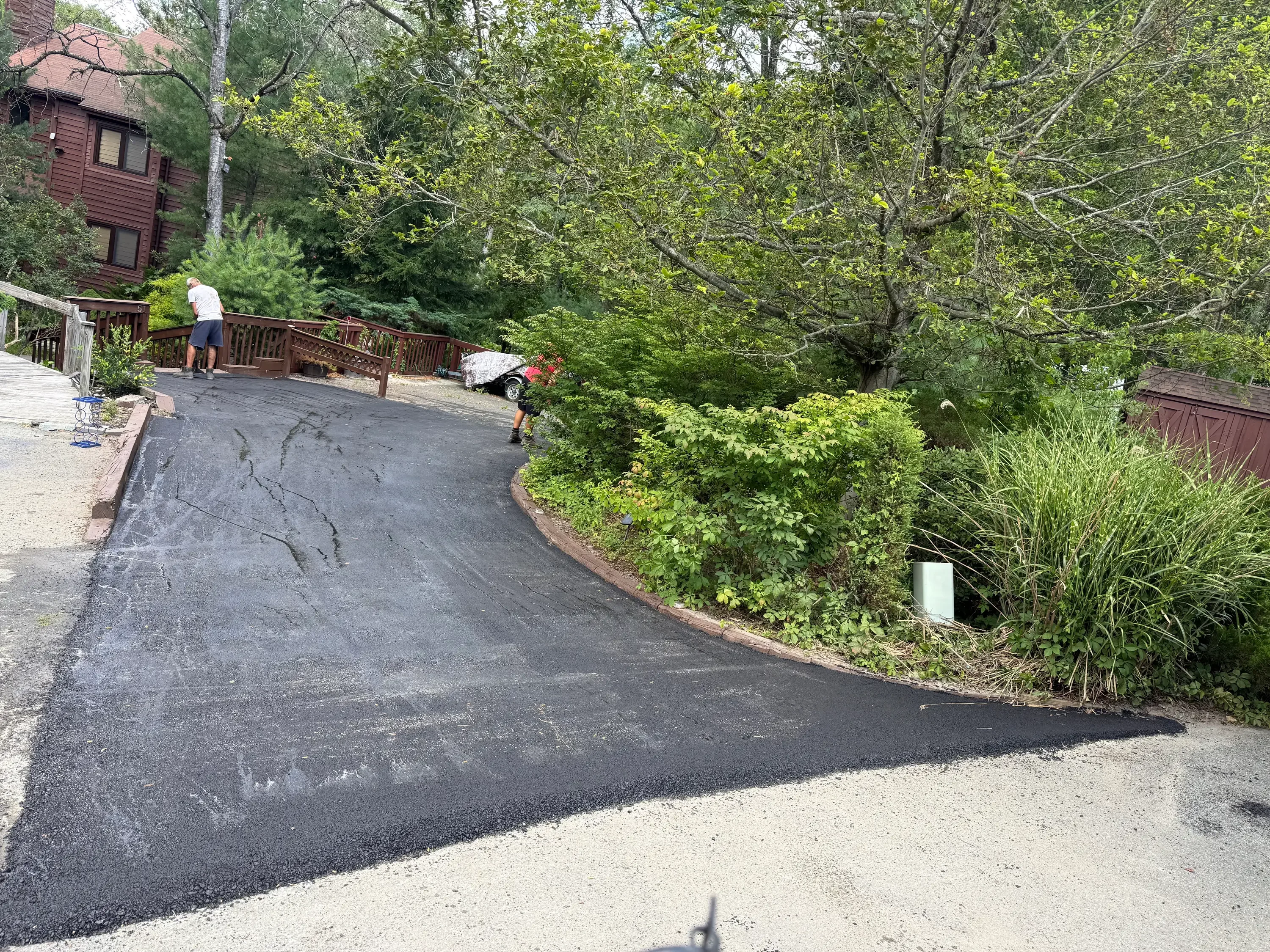 Newly paved asphalt driveway with curved layout and brick border edging