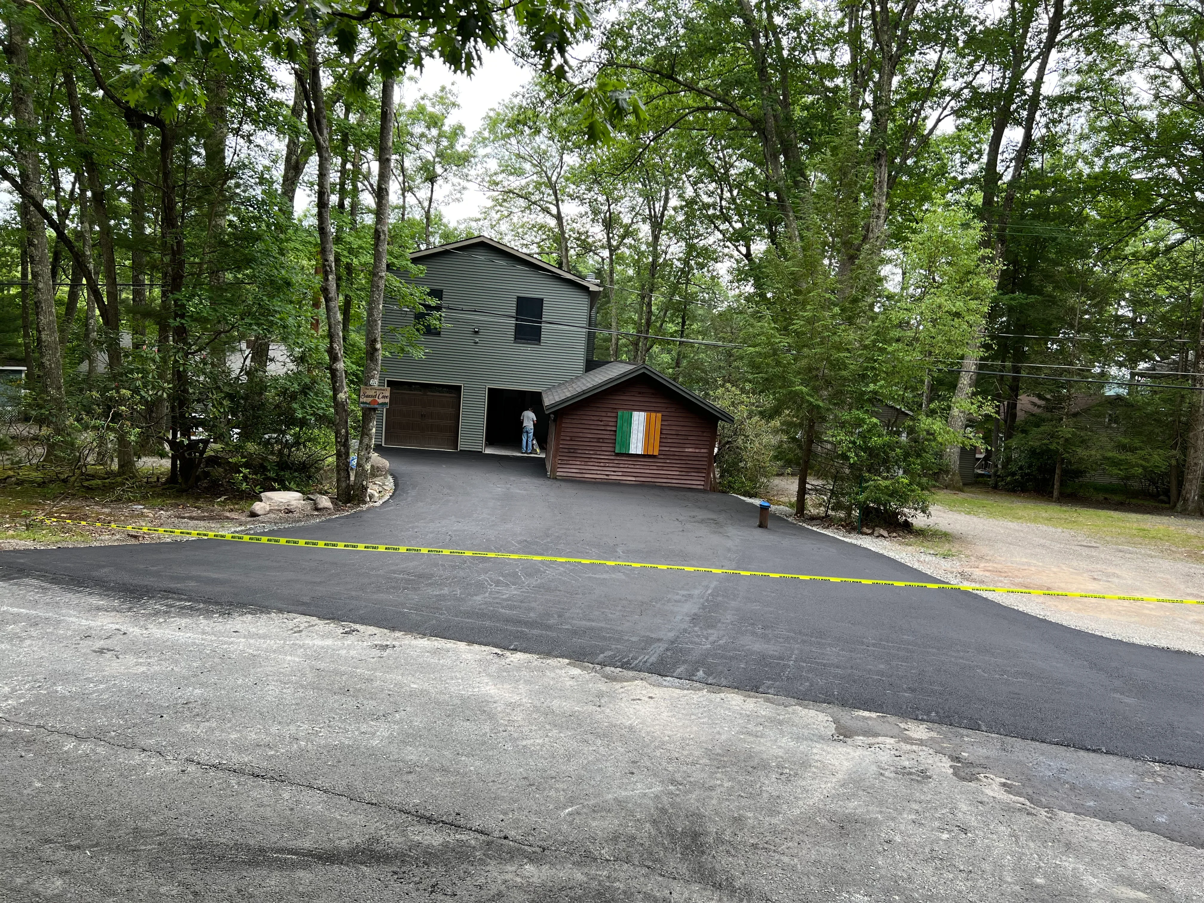 New black asphalt driveway leading to residential garage in wooded setting