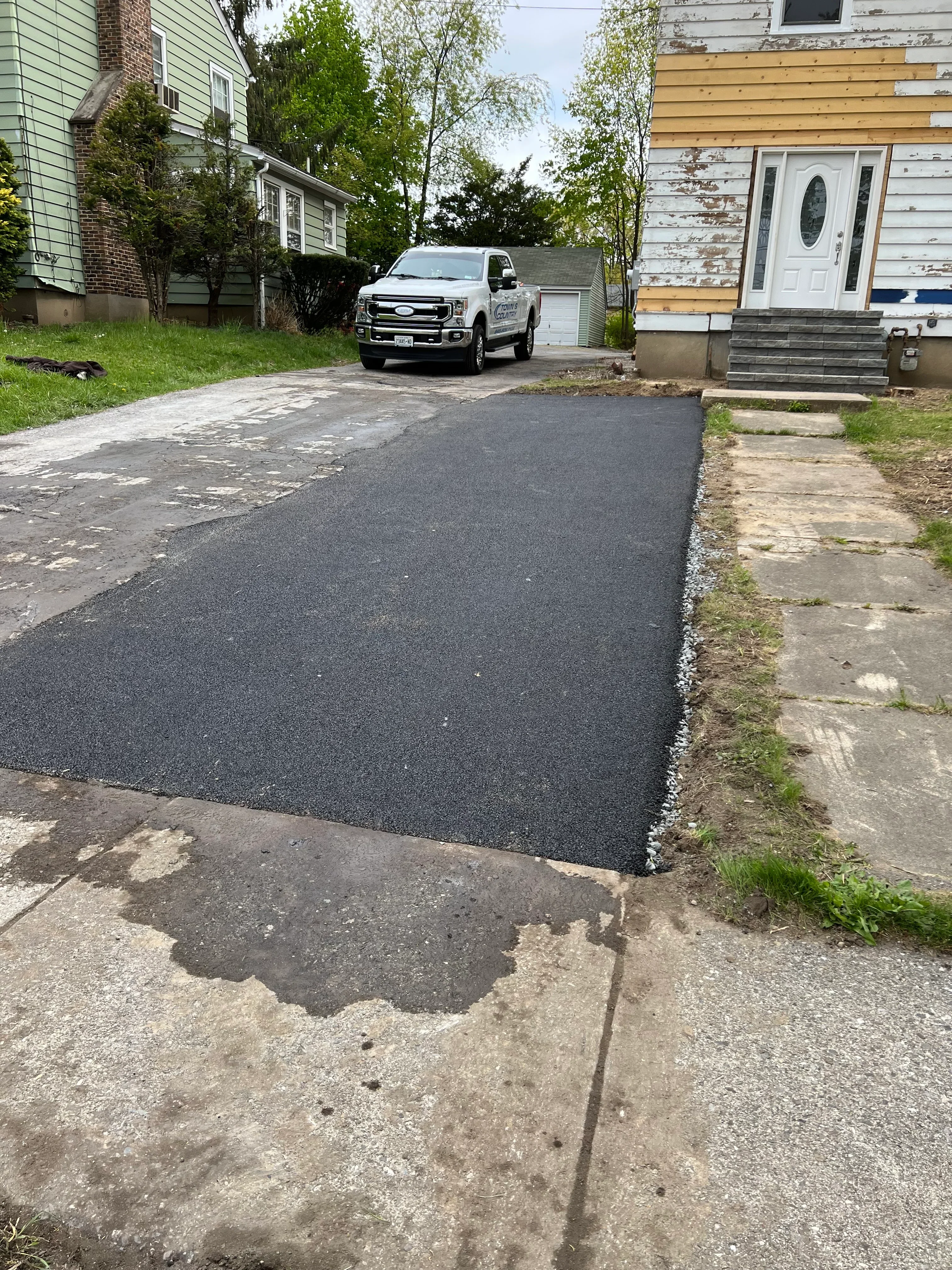 Newly paved asphalt driveway with dark surface and clean edges adjacent to concrete
