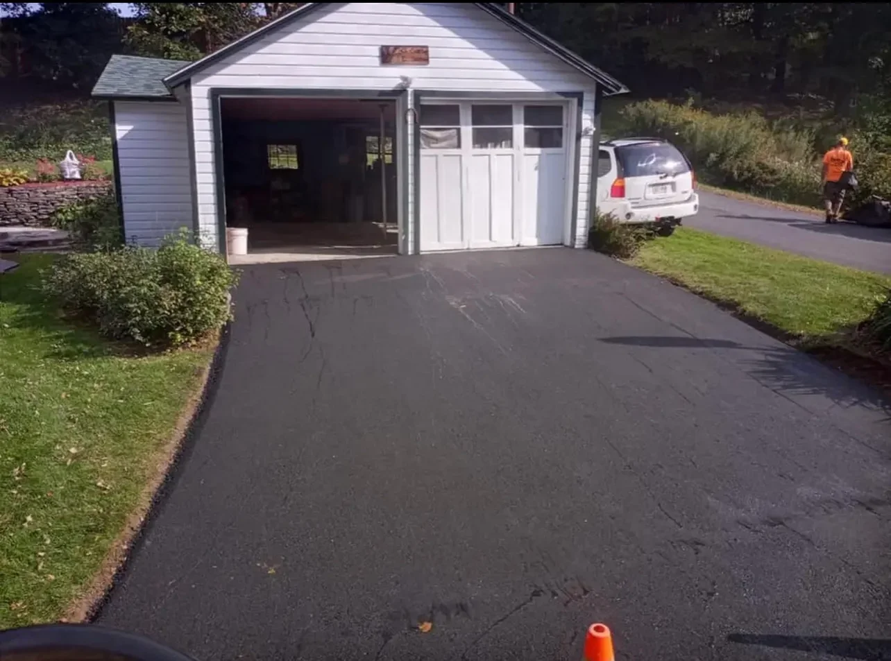 Newly paved black asphalt driveway in front of white two-car garage