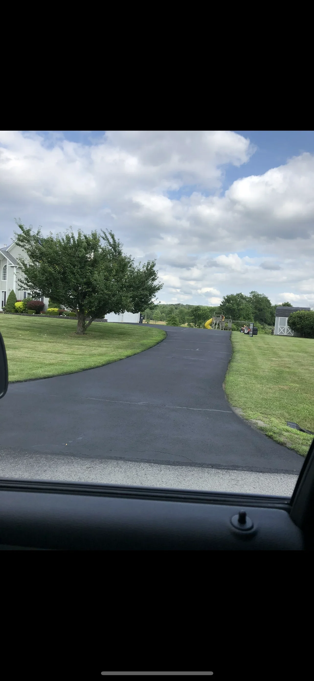 Newly paved curved asphalt driveway with manicured lawn borders and mature trees